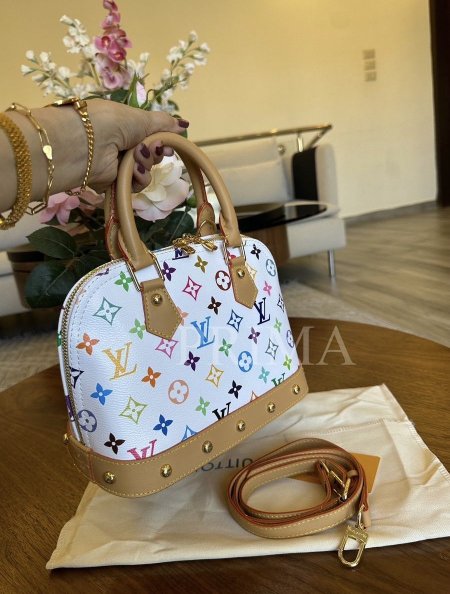 حقيبة "Louis Vuitton x Takashi Murakami Alma BB" وهي قطعة مميزة من مجموعة محدودة. تحتوي على مقبضين علويين من جلد التورون، وحزام كتف قابل للإزالة. لونها الأساسي أبيض مع نقوش مونوغرام بألوان متعددة. جودة اللون عالية مختومة قاعدة 25 سم